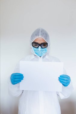 Female doctor with protective workwear holding empty cardboard while standing at clinic and looking at camera. Copy space.