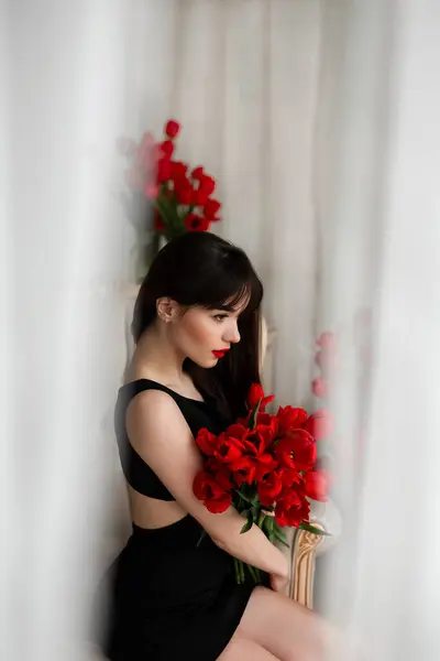 花を持った魅力的な若い女性 チューリップの花束を持つ美しいブルネットの少女 チューリップを保持する美しい官能的な女性 ストック画像