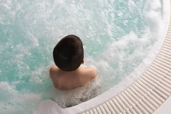 暖かい泡立つ水ジャグジーに座っている少年 スパでリラックスできるハッピーガール トップビュー ストック写真