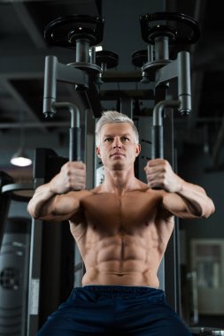 Kendini adamış ve formda bir adam modern bir spor salonunda spor aletleri üzerinde çalışıyor, atletizm ve kararlılığını gösteriyor.