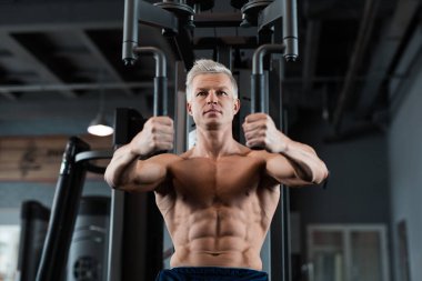 Kendini adamış ve formda bir adam modern bir spor salonunda spor aletleri üzerinde çalışıyor, atletizm ve kararlılığını gösteriyor.