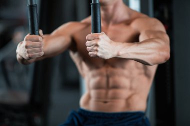 Kendini adamış ve formda bir adam modern bir spor salonunda spor aletleri üzerinde çalışıyor, atletizm ve kararlılığını gösteriyor.