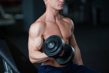 Formda bir adam modern bir spor salonunda dambılları kaldırıp formda olduğunu göstererek güç ve kararlılık gösterir.