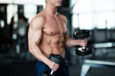 Formda bir adam modern bir spor salonunda dambılları kaldırıp formda olduğunu göstererek güç ve kararlılık gösterir.