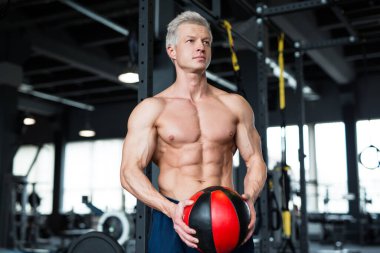 Bir adam profesyonel bir spor salonunda kettlebell egzersizi yaparken görülüyor. Gücünü ve vücut geliştirmeye odaklanıyor.