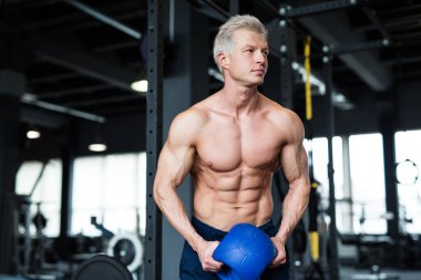 Bir adam profesyonel bir spor salonunda kettlebell egzersizi yaparken görülüyor. Gücünü ve vücut geliştirmeye odaklanıyor.
