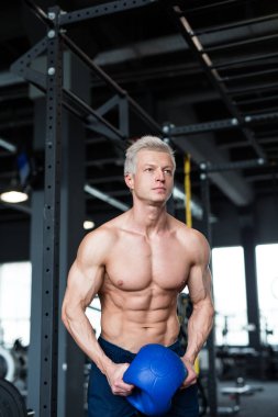 Bir adam profesyonel bir spor salonunda kettlebell egzersizi yaparken görülüyor. Gücünü ve vücut geliştirmeye odaklanıyor.