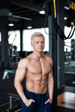 Atletik bir adam kaslarını ve kaslarını kapalı bir spor salonunda sergiliyor.