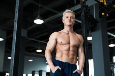 Atletik bir adam kaslarını ve kaslarını kapalı bir spor salonunda sergiliyor.