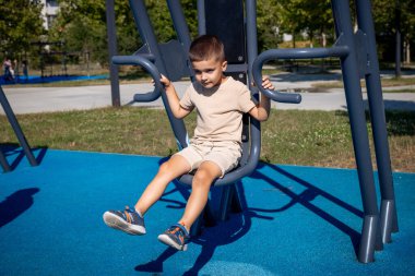 Neşeli bir çocuk dışarıda oyun ekipmanlarıyla oynayarak harika vakit geçiriyor. Parkta güneşli bir günün tadını çıkarıyor.
