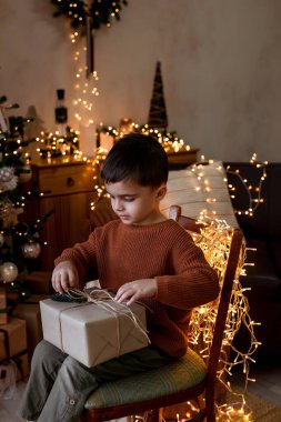 Genç bir çocuk, büyüleyici ve büyüleyici Noel süslemelerinin arasında güzel bir hediye açar.