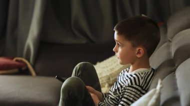 Beyaz çocuk kanepede oturup oturma odasında televizyon izliyor. Odaklanmış esmer bir gencin akşam evde televizyon karşısında oturup film izlemesinin yan görüntüsü..