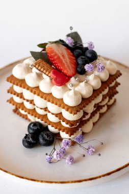 Çıtır bisküviler, krema, taze böğürtlen ve çiçeklerle süslenmiş sofistike katmanlı bir pasta..