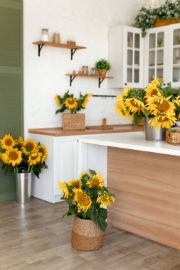 Beyaz dolapları, ahşap aksanları ve canlı ayçiçekleri olan yeni, modern bir mutfak. Sallanan ışıklar ve yeşillik sıcaklık ekler, rahat ve davetkar bir yer yaratır..