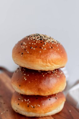 Üzerinde susam ve siyah tohumlar olan kahverengi brioche çörekleri, rustik bir tahta üzerine yerleştirilmiş. Yumuşak, yumuşak ve sandviç ve hamburger için mükemmel..