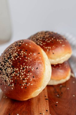 Üzerinde susam ve siyah tohumlar olan kahverengi brioche çörekleri, rustik bir tahta üzerine yerleştirilmiş. Yumuşak, yumuşak ve sandviç ve hamburger için mükemmel..