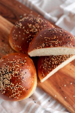 Üzerinde susam ve siyah tohumlar olan kahverengi brioche çörekleri, rustik bir tahta üzerine yerleştirilmiş. Yumuşak, yumuşak ve sandviç ve hamburger için mükemmel..