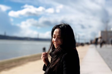 Huzurlu bir kadın, güzel bulutlu bir gökyüzü tarafından güzel çerçevelenmiş sakin suyun yanında keyifli bir anın tadını çıkarıyor.