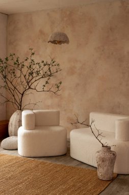 Yumuşak krem mobilyalar, toprak dokular ve büyük seramik vazolardaki dallar gibi doğal elementlerin yer aldığı rahat, minimalist bir oturma odası..