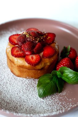 Taze çilek, pudra şekeri ve fesleğen yapraklarıyla kaplı lezzetli bir mini pasta, yumuşak pembe bir tabakta güzelce servis edilir..