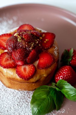 Taze çilek, pudra şekeri ve fesleğen yapraklarıyla kaplı lezzetli bir mini pasta, yumuşak pembe bir tabakta güzelce servis edilir..