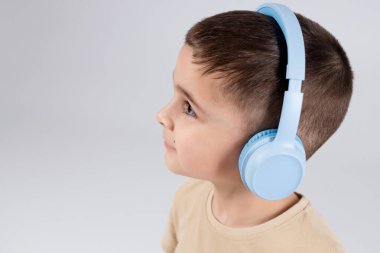Parlak mavi kulaklıklı, bej gömlekli, müzik dinleyen neşeli bir gencin yakın plan portresi..