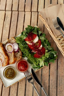 Domatesli Caprese salatası, mozzarella, taze yeşiller, zanaatkar ekmek dilimleri, kırmızı soğan halkaları ve iki aromalı sos içeren canlı bir tabak..