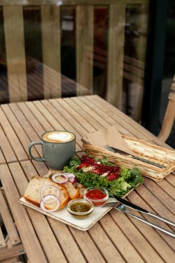Caprese salatası, soğan halkalı taze ekmek, pesto ve domates sosu ve kremalı latte içeren sıcak bir kafe brunch 'ı..