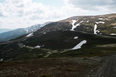 Svydovets sıradağlarındaki karlı dağların çarpıcı manzarası, batı Ukrayna, engebeli araziler ve parçalı bulutlu gökyüzü altında yemyeşil alanlar..