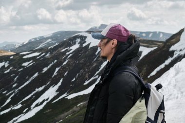 Siyah ceketli ve pembe şapkalı bir yürüyüşçü karlı bir dağ yolunda duruyor, Svydovets dağlarındaki manzaralı Karpatlar tepelerine bakıyor..