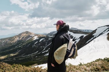 Kırmızı şapkalı snowboardcu, batı Ukrayna 'daki Svydovets dağ sırasındaki karlı tepelere bakan teçhizatlar taşıyor..