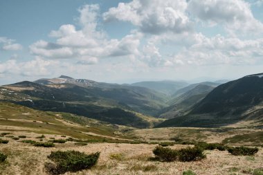 Batı Ukrayna 'nın Svydovets bölgesindeki parçalı bulutlu gökyüzünün altında engebeli dağlarla çevrili yemyeşil bir vadinin geniş manzarası..