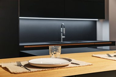 Siyah bir mutfak setinin arka planında tabak ve cam var.