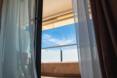 Mavi gökyüzü açık balkon kapısından görünüyor.