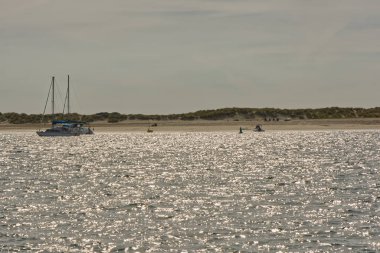 Doğu Kafası 'nda demirli tekneler, Chichester Limanı' nda Batı Wittering, Batı Sussex, İngiltere. Tanınmayan insanlar sahilde eğlenirken..