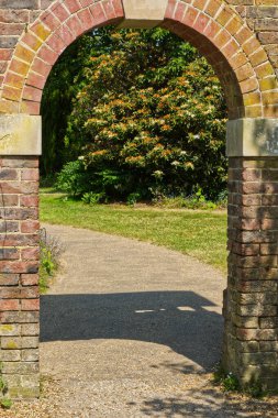 İngiliz kır bahçesindeki eski tuğla duvarda kemerli kapı..