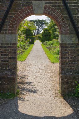Eski tuğla duvardaki kemerli kapı İngiliz kır bahçesine açılıyor..
