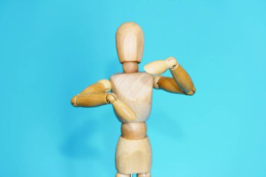 Sarı ahşap manken mavi arka planda el hareketlerini gösteriyor.