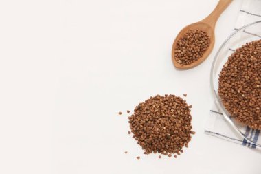 Tahta bir kaşık ve cam bir tabakta doğal kahverengi karabuğday taneleri.