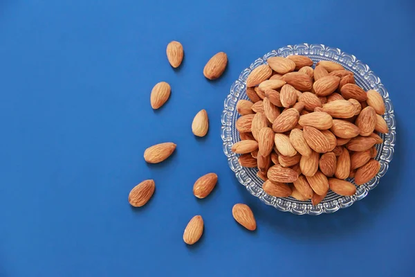 Mavi arka planda şeffaf bir tabakta kurumuş kahverengi badem taneleri.