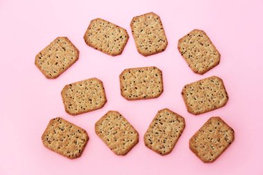 Kare kuru krakerler ve pembe arka planda beslenme tohumları.