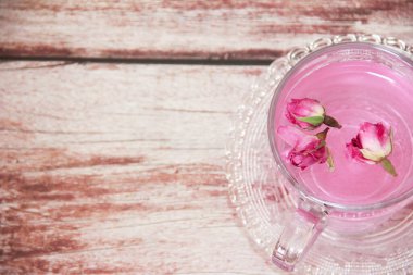 Pembe çay, doğal kuru gül tomurcuklarıyla şeffaf bir kupada, ahşap bir arka planda.