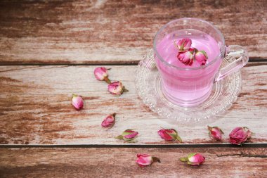 Pembe çay, doğal kuru gül tomurcuklarıyla şeffaf bir kupada, ahşap bir arka planda.