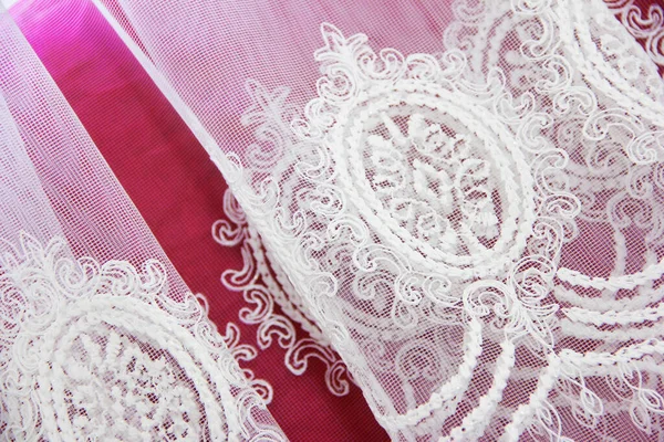 texture of white decorative lace fabric with floral ornament on pink background