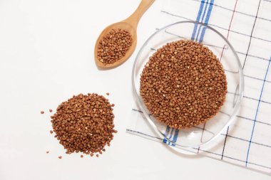 Şeffaf cam tabakta ve tahta kaşıkta küçük kahverengi doğal karabuğday taneleri.