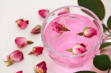 Beyaz arka planda şeffaf bir fincanda kurumuş küçük gül goncalarından yapılmış pembe çay.