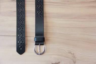 Ahşap bir arka planda dekoratif süslemeli siyah deri kadın pantolon kemeri.