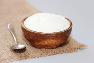 Tahta bir tabakta, metal bir kaşığın yanında, doğal mayalanmış süt yoğurdu.