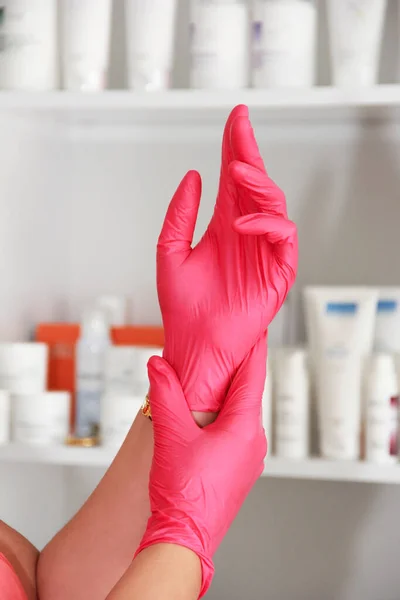 The hands of a cosmetologist doctor in pink gloves on the background of medical preparations