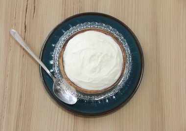 Dekoratif bir tabakta beyaz mayalanmış süt yoğurdu ve tahta bir arka planda metal kaşık.